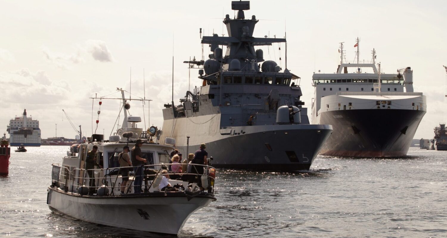 Unter großem Medieninteresse geleitet die Korvette Braunschweig das RoRo-Schiff Ark Germania im Rahmen der Übung Quadriga 2025 aus dem Rostocker Hafen.