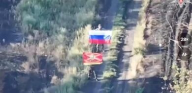 Lächeln für die Drohne: Zwei russische Soldaten posieren mit Flaggen für ein Beweisfoto von der Eroberung eines Dorfes in der Ukraine.
